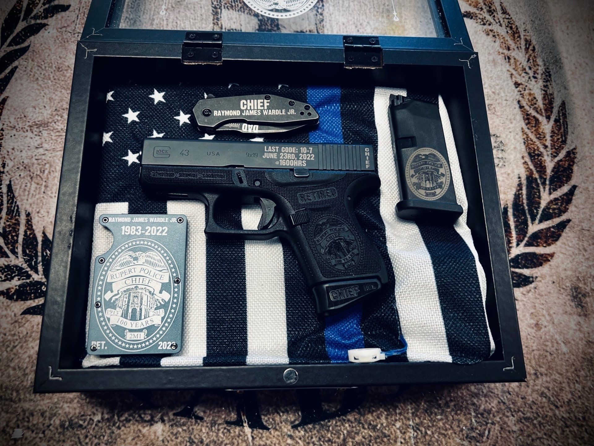 Display case with handgun, knife, magazine, and wallet on a blue line American flag.