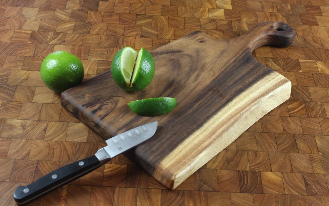 Limes and a knife on a wooden cutting board with one lime sliced in half.