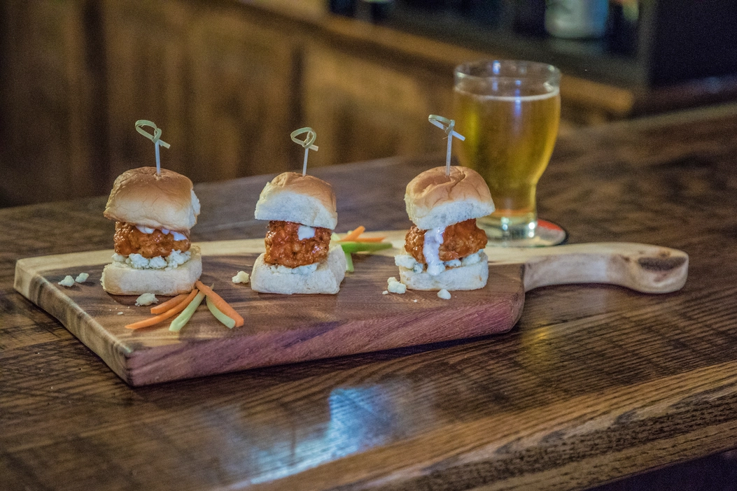 Three mini sliders on a wooden board with fries and a beer on a rustic table.