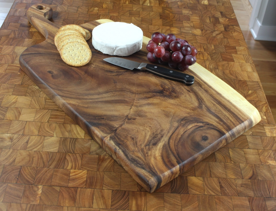 Wooden cutting board with sliced bread, white cheese, red grapes, and a knife on a kitchen counter.