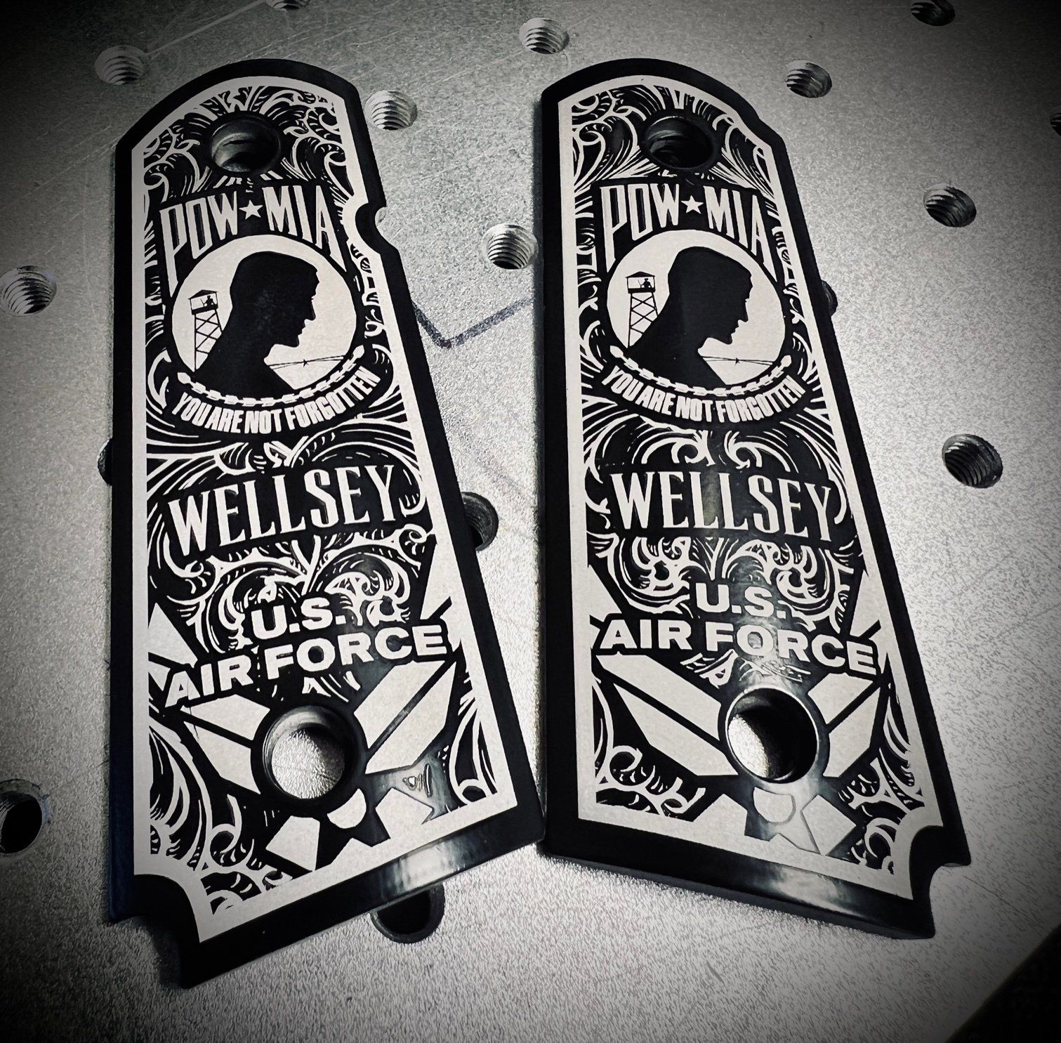 Two custom handgun grips, black and white, engraved with a POW-MIA design, a man's silhouette, and 