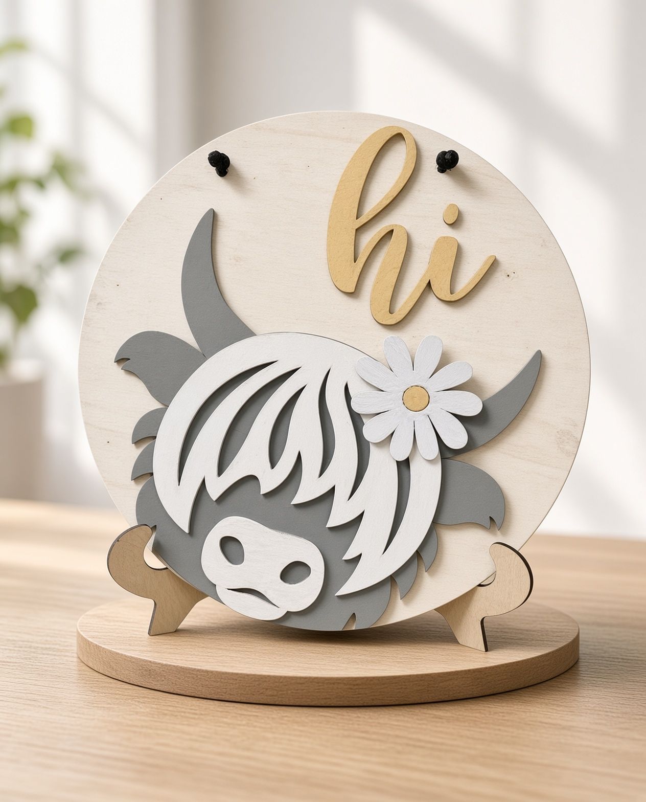 Wooden circular sign with a gray donkey, gold “hi,” and a white flower on a speckled surface.