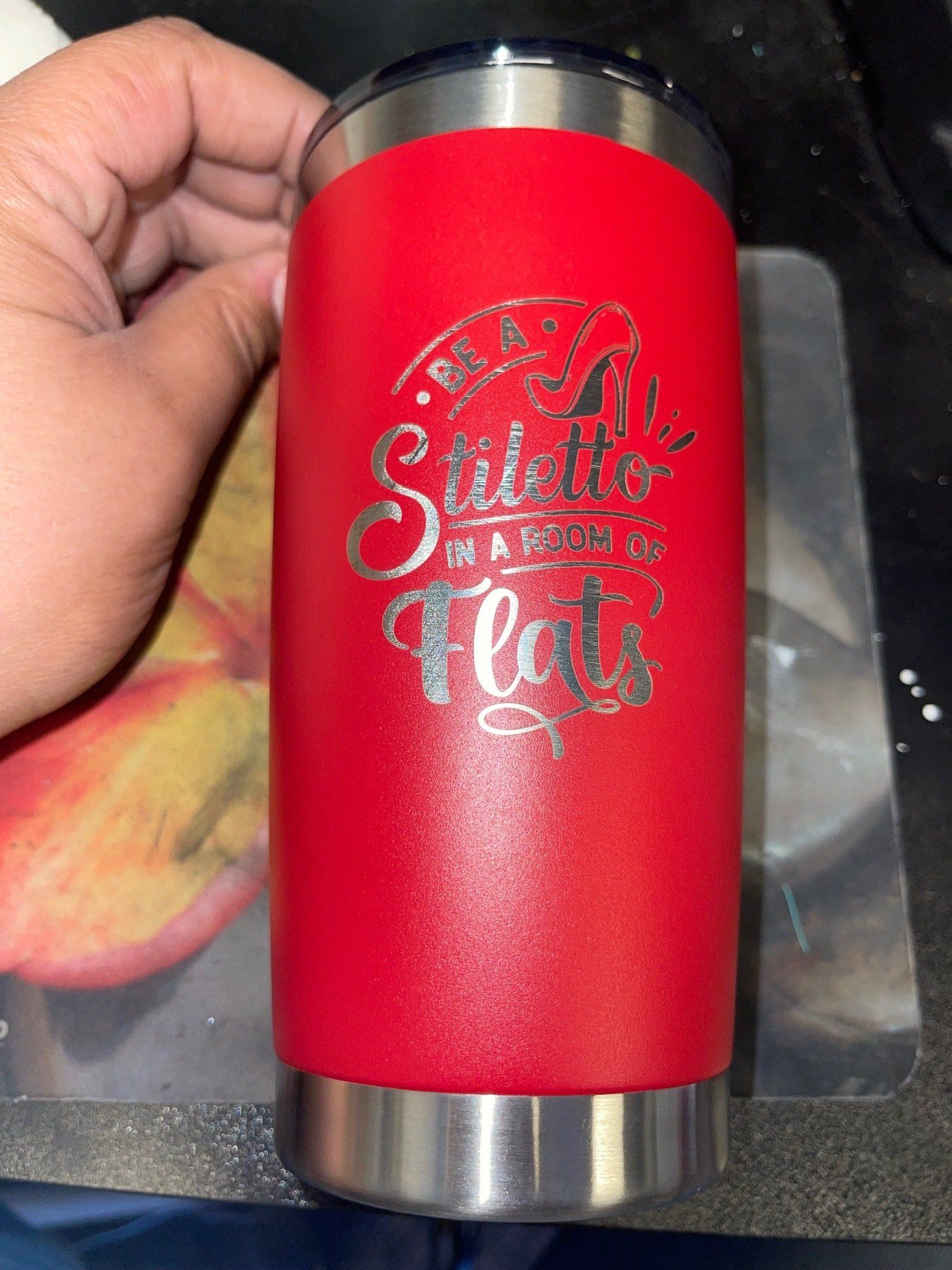 Red insulated tumbler with silver lid and base, held in a hand, with decorative white script on the front