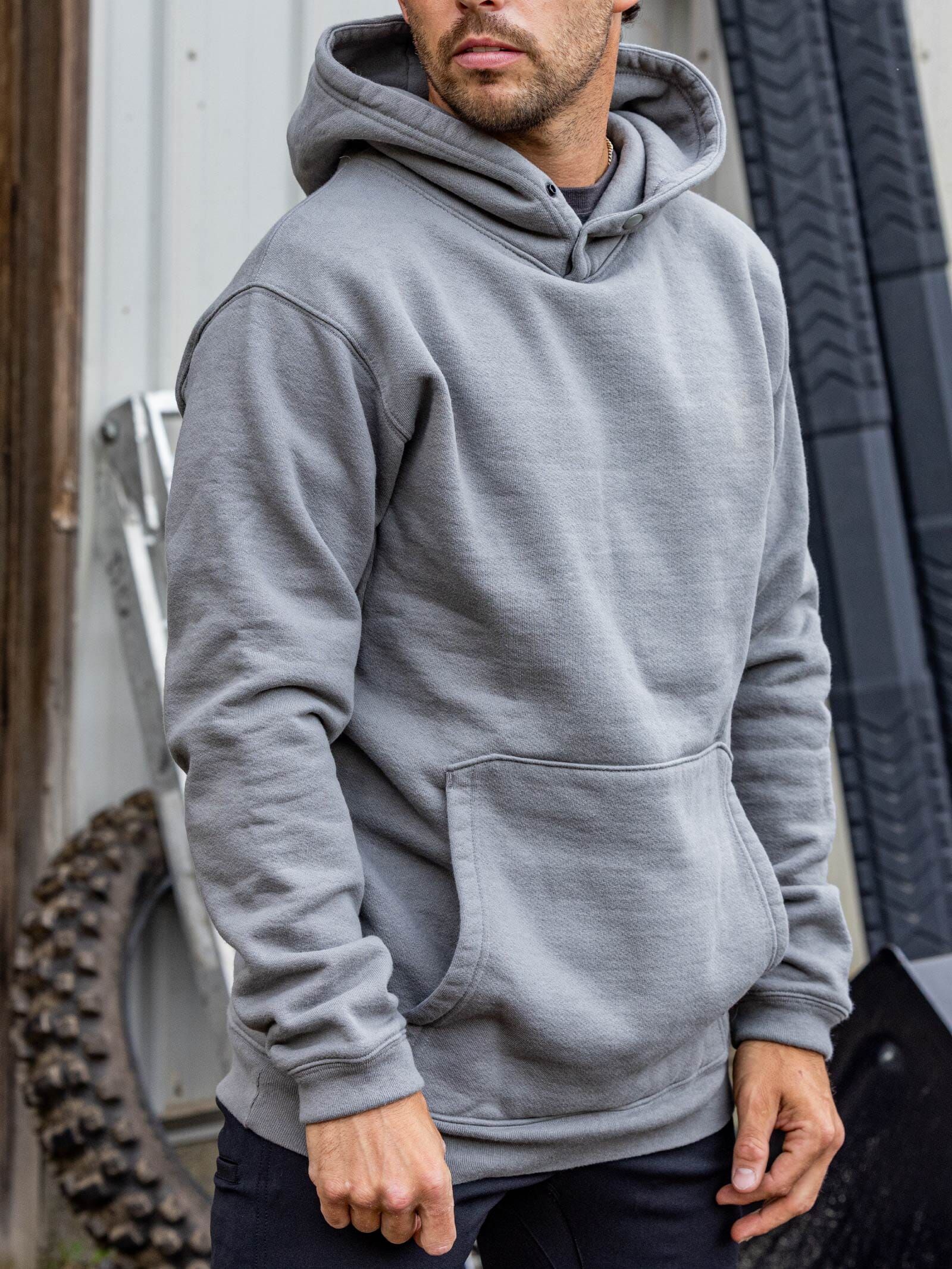 Man in a gray hoodie standing outdoors beside industrial metal equipment
