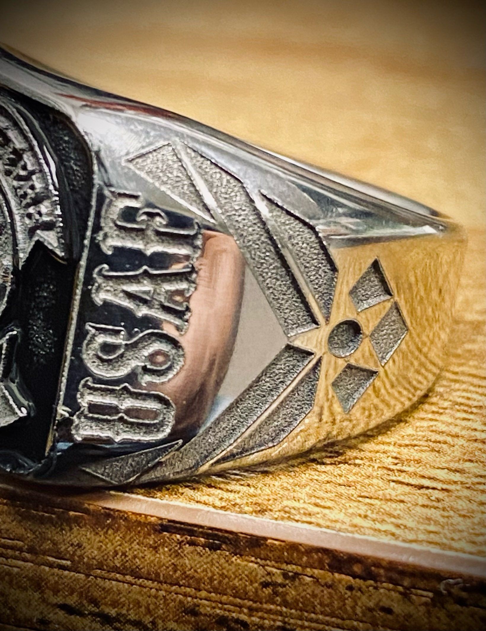 Close-up of a silver ring with engraved lettering and a star emblem on a wooden surface.