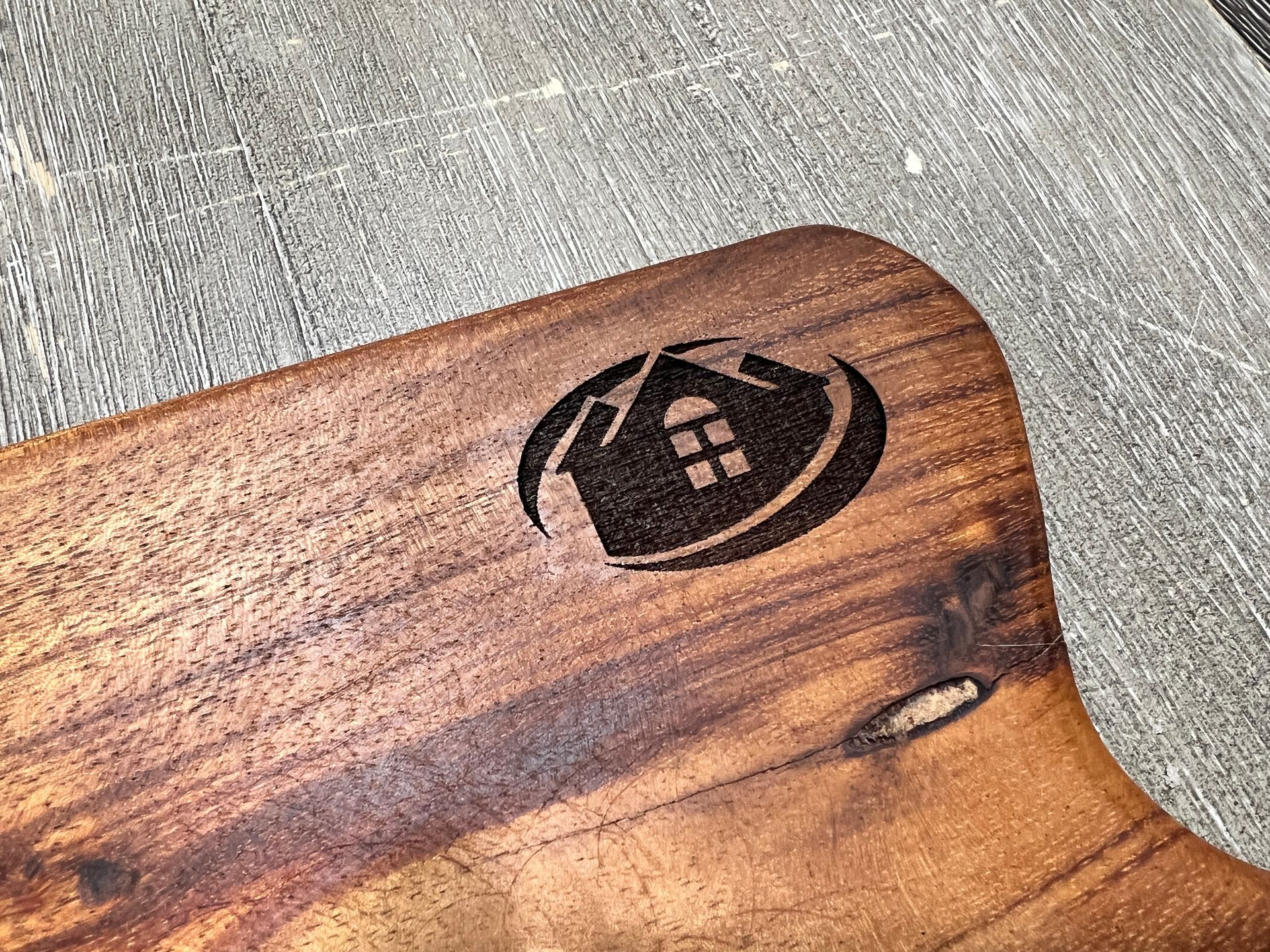 Wooden cutting board with a laser-etched house logo.