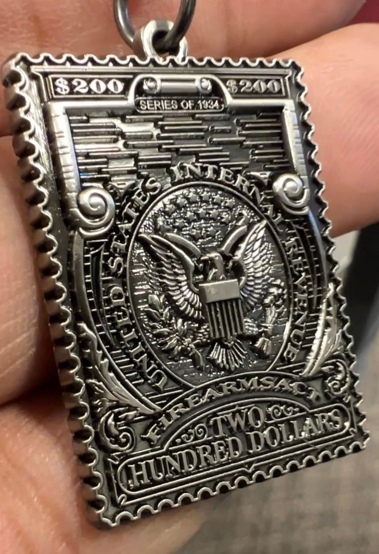 Silver-colored pendant shaped like a stamp. Features 