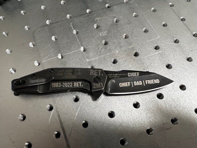 Black folding knife with engraved text: 