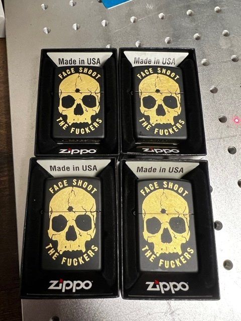 Four black Zippo lighters with skull design and text: 