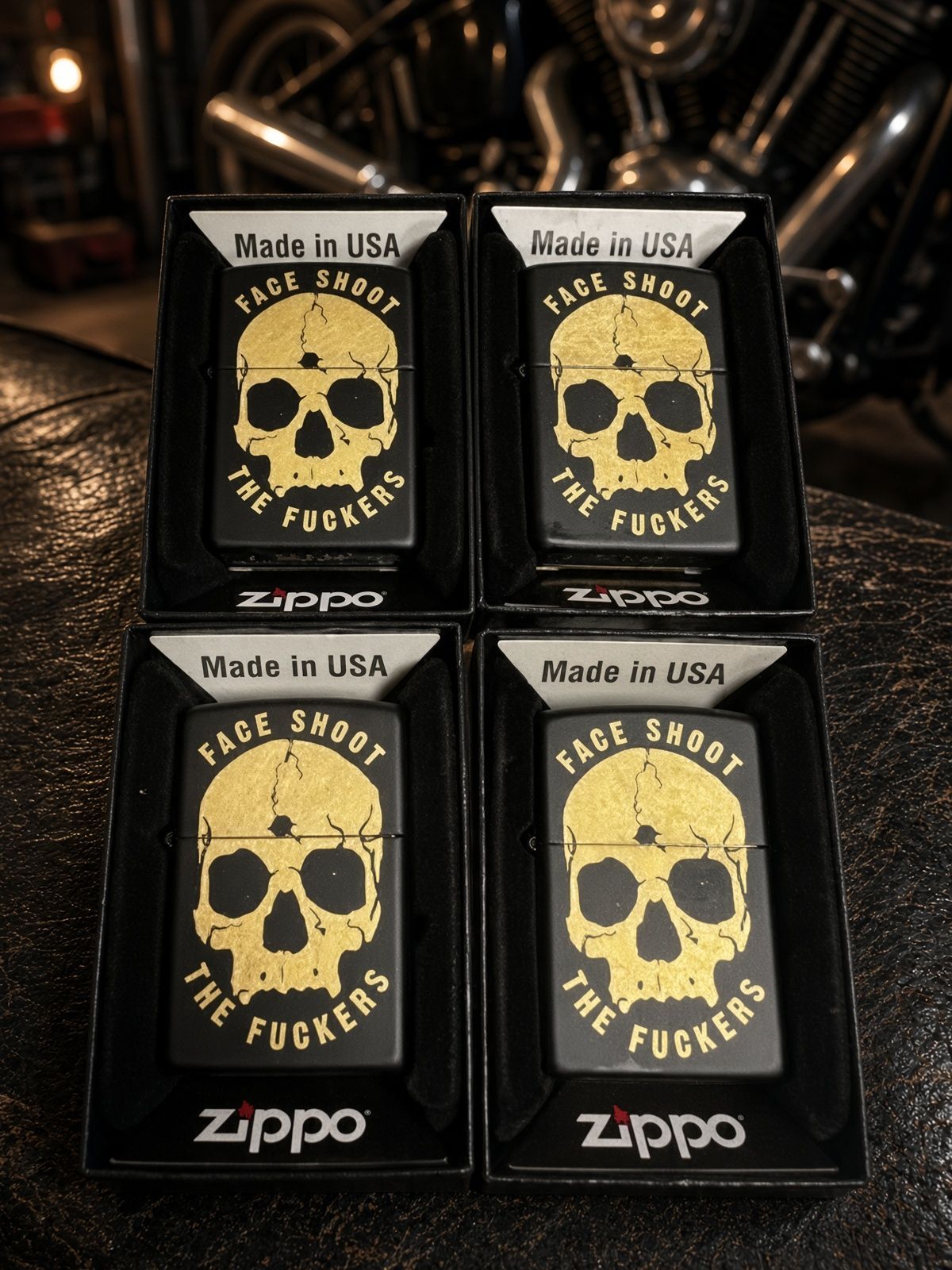 Four black Zippo lighters with yellow skull-and-text designs arranged in a 2x2 grid on a beige surface
