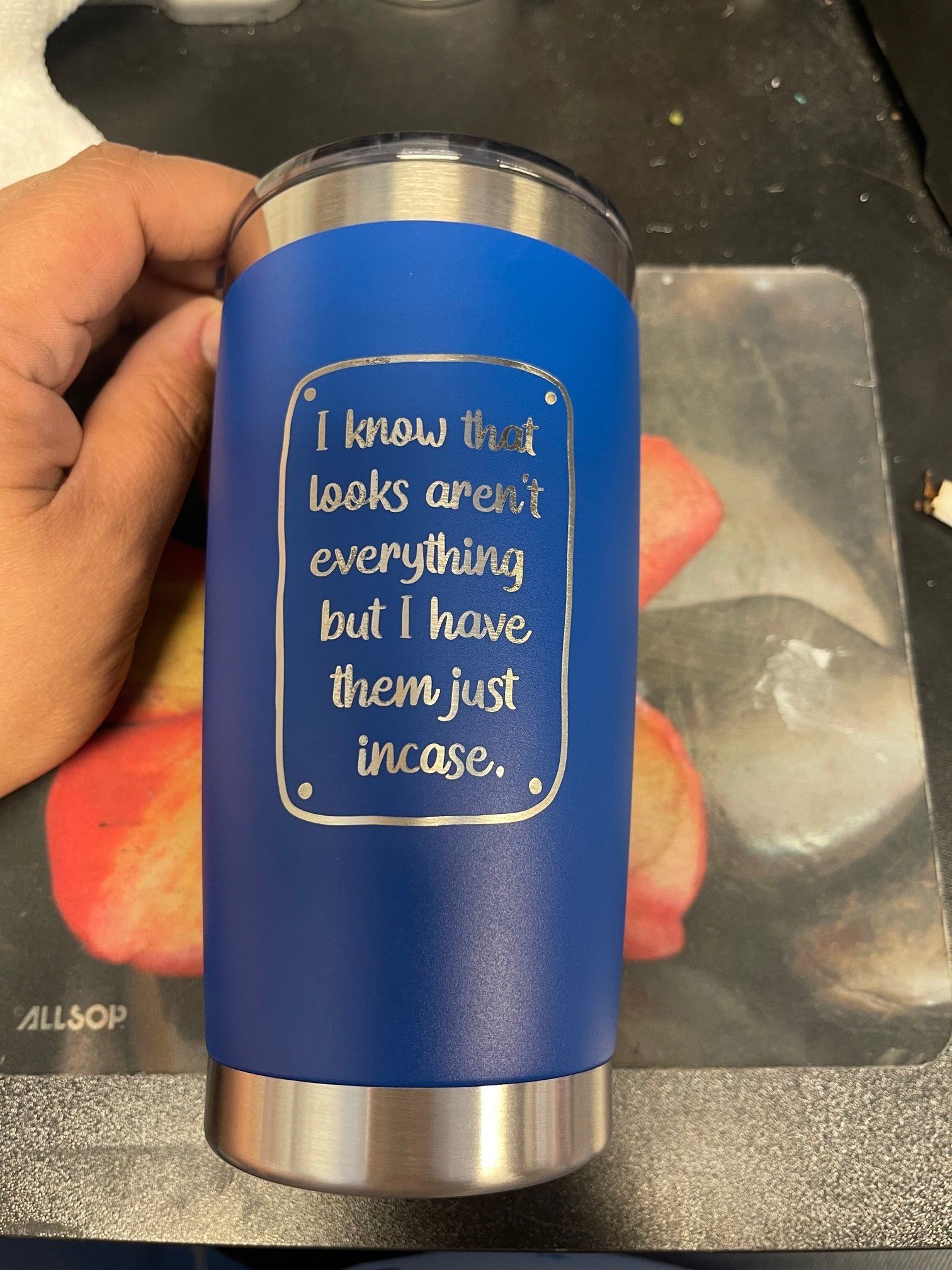 Blue tumbler with a white handwritten quote held in a hand on a countertop.