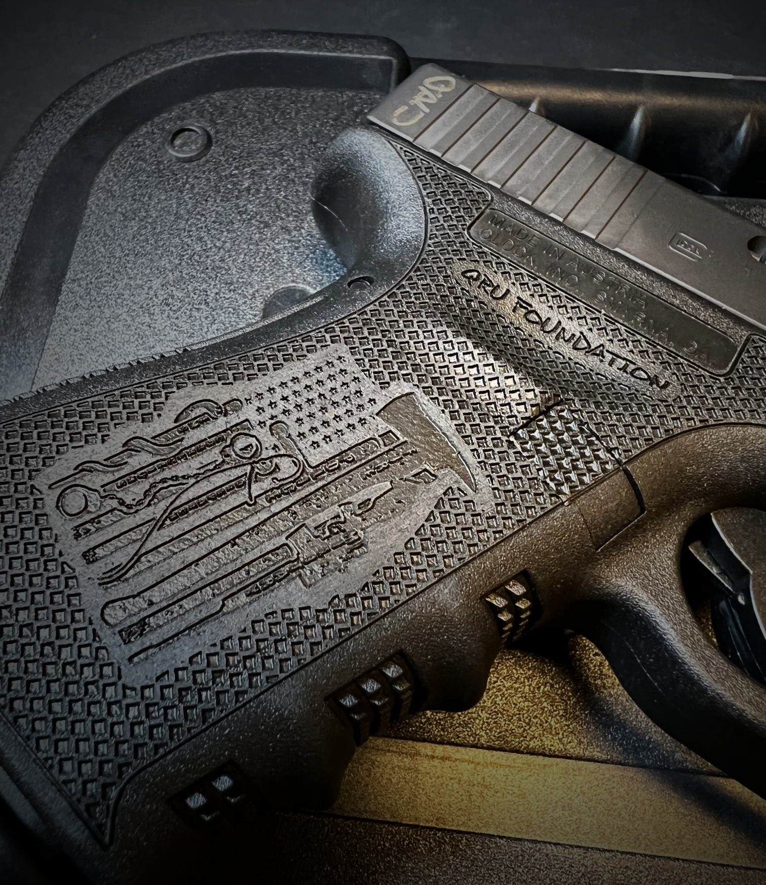 Close-up of a black semi-automatic pistol with a textured grip and engraved slide on a dark surface