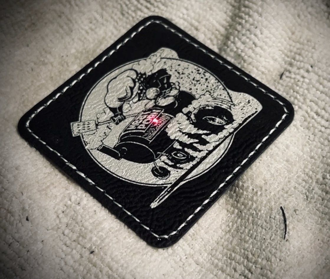 Black patch with a white cartoon skull design and pink accent, stitched onto light fabric.