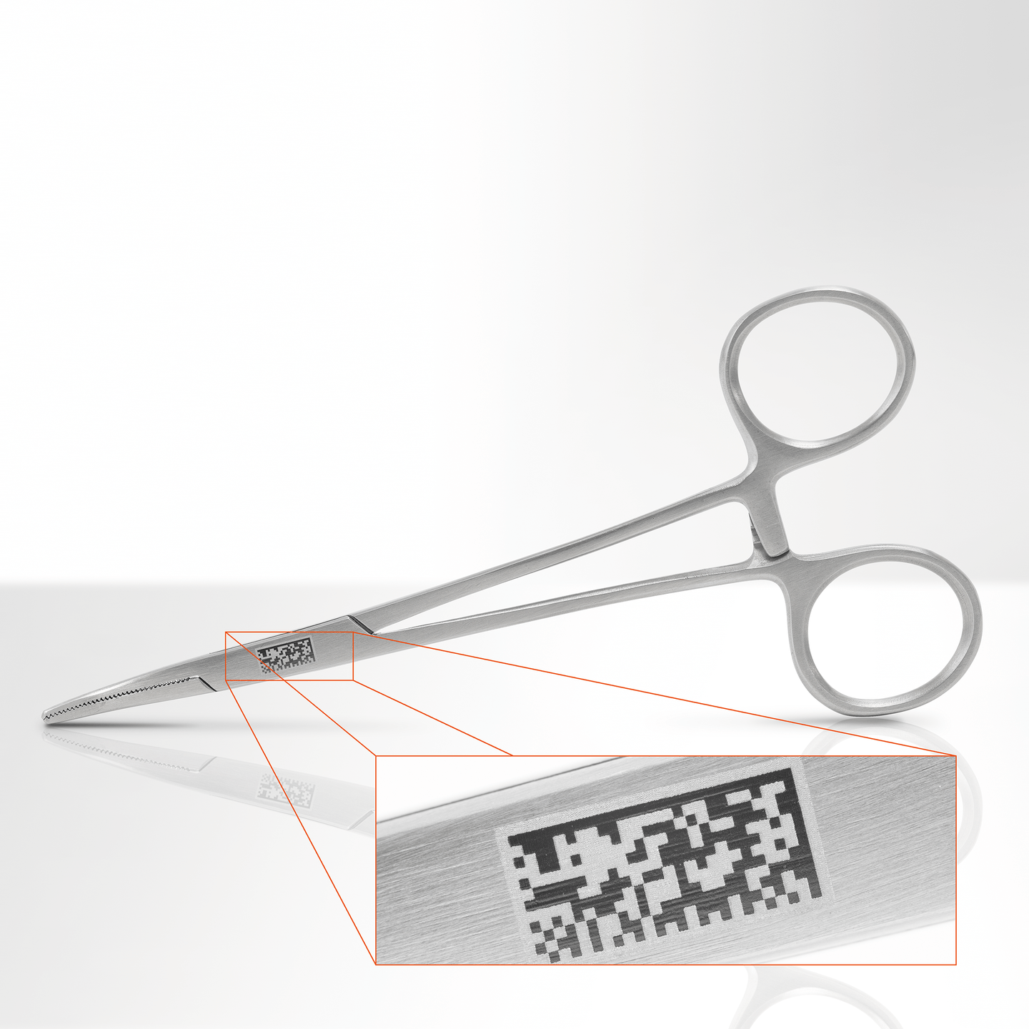 Gray surgical forceps holding a small block, with a magnified close-up inset of its textured surface.