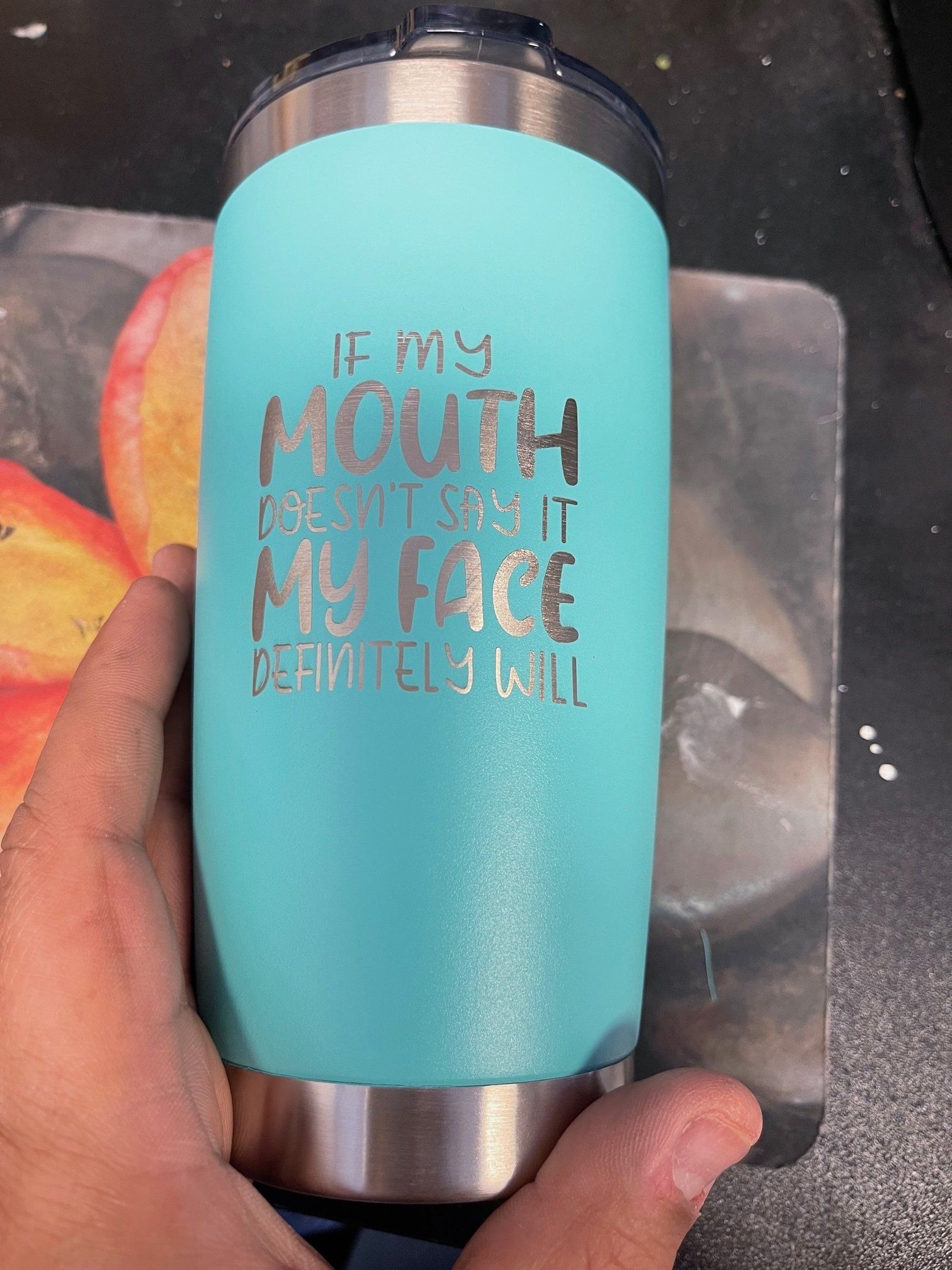 Turquoise insulated tumbler with quote, held in a hand on a countertop.