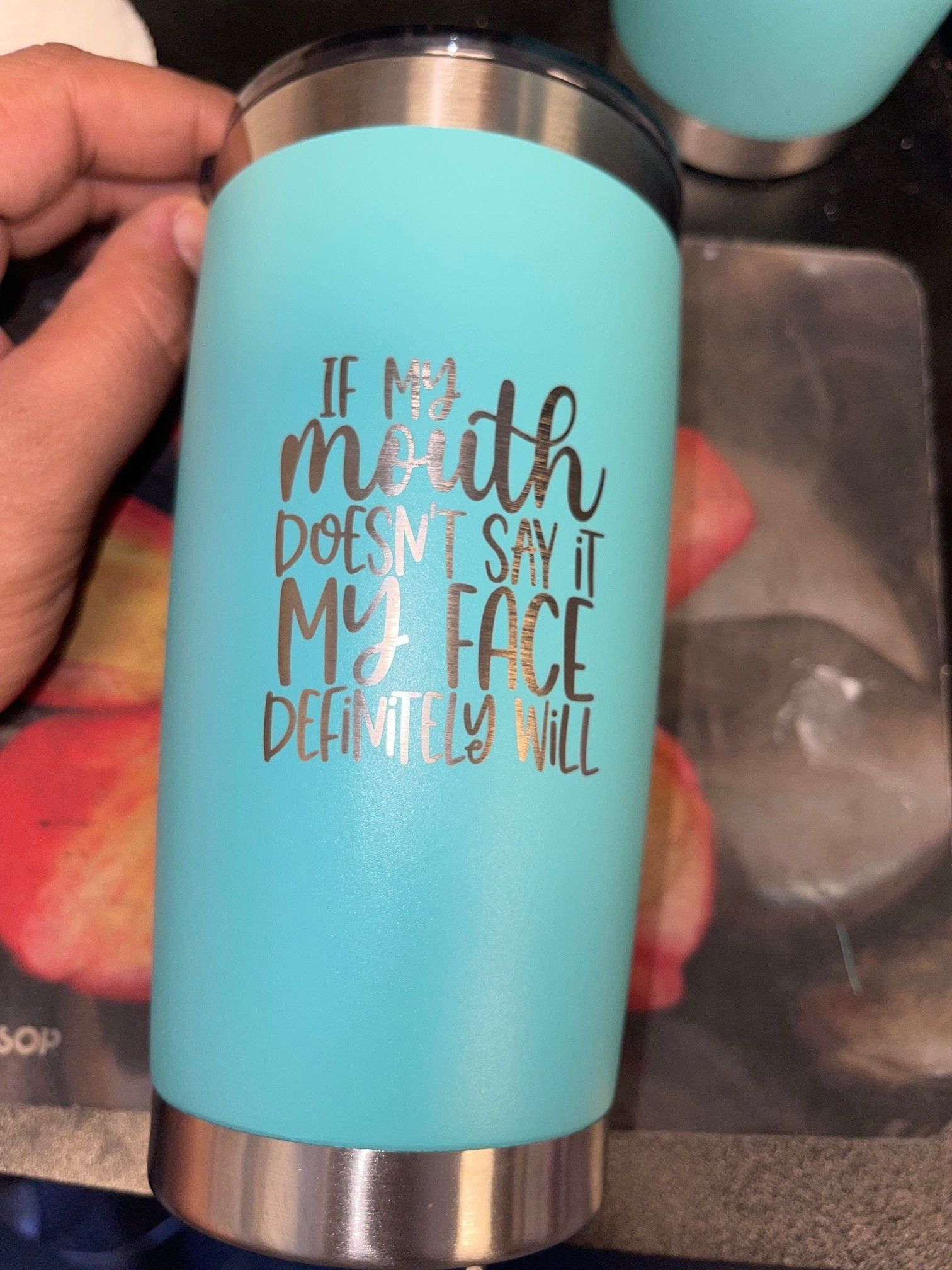 Turquoise tumbler with metallic top and bottom, held in a hand, with a motivational quote printed on it.