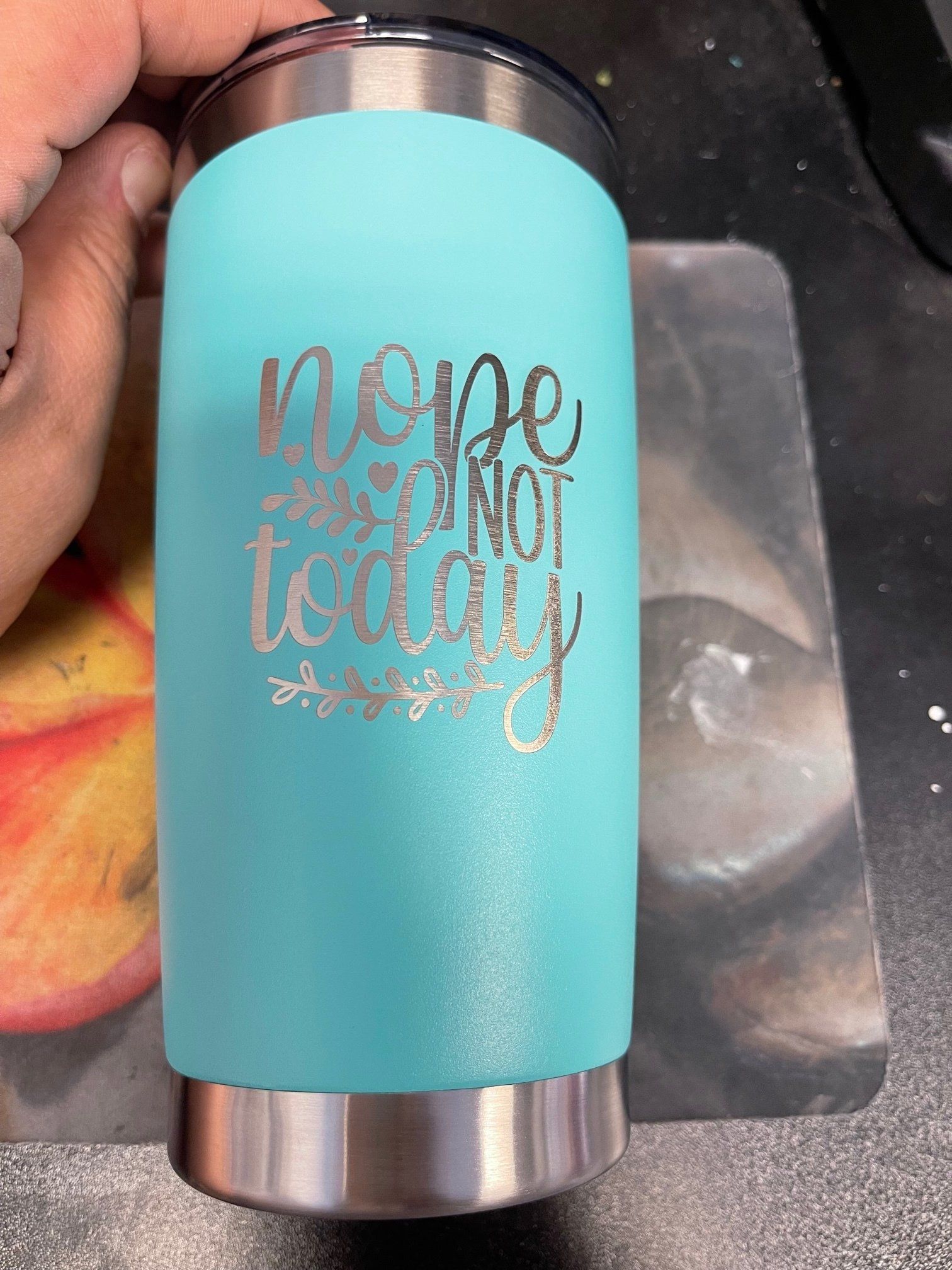 Turquoise insulated tumbler with metallic script on a hand over a sink.