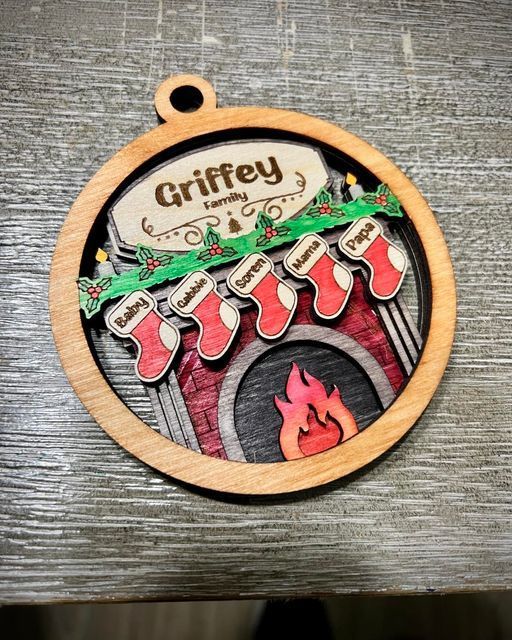 Round wooden Christmas ornament with a fireplace, stockings, and “Grifey” text on a gray background