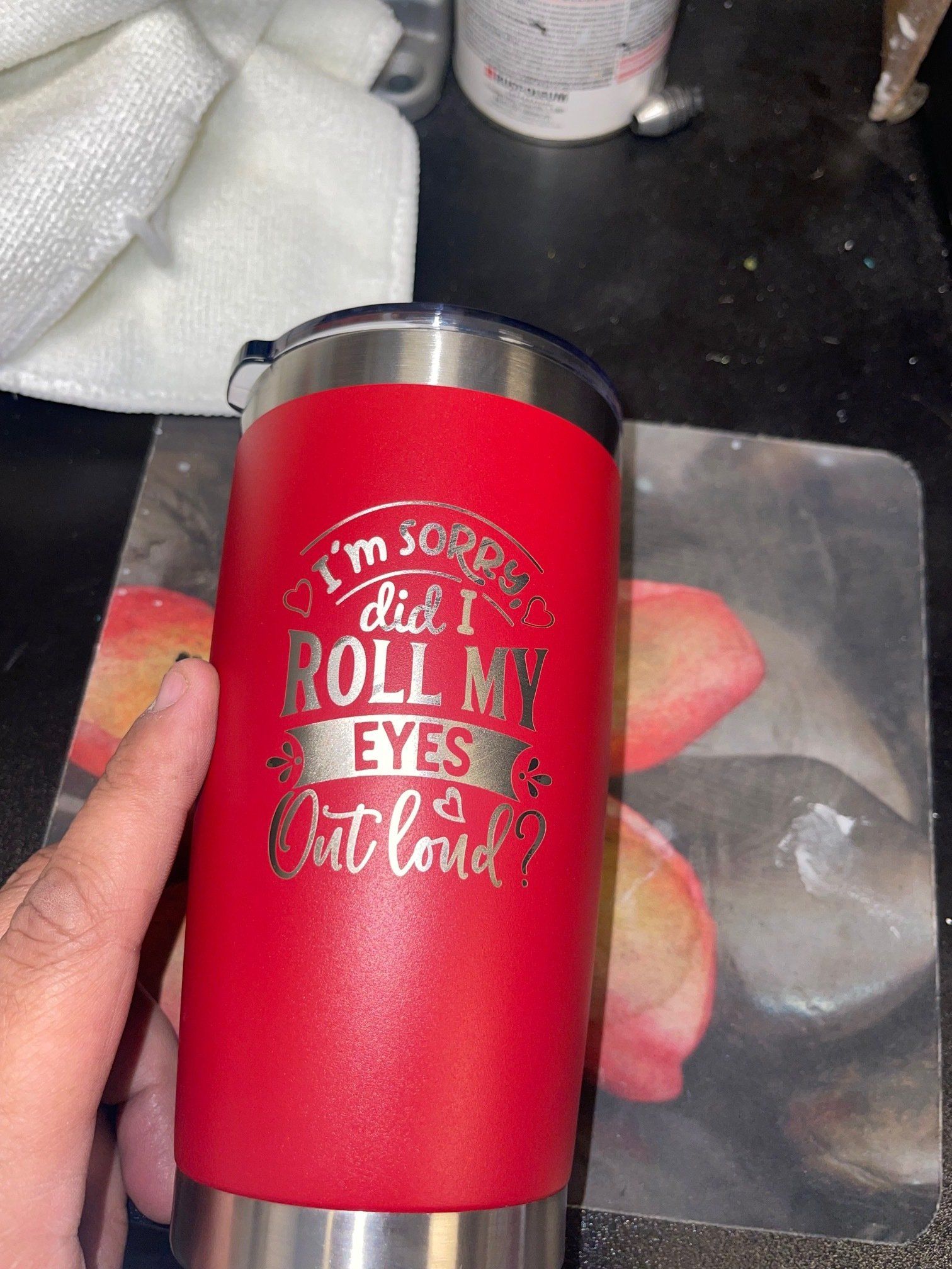 Red tumbler with white quote on countertop, beside a plastic bag and paper towel.