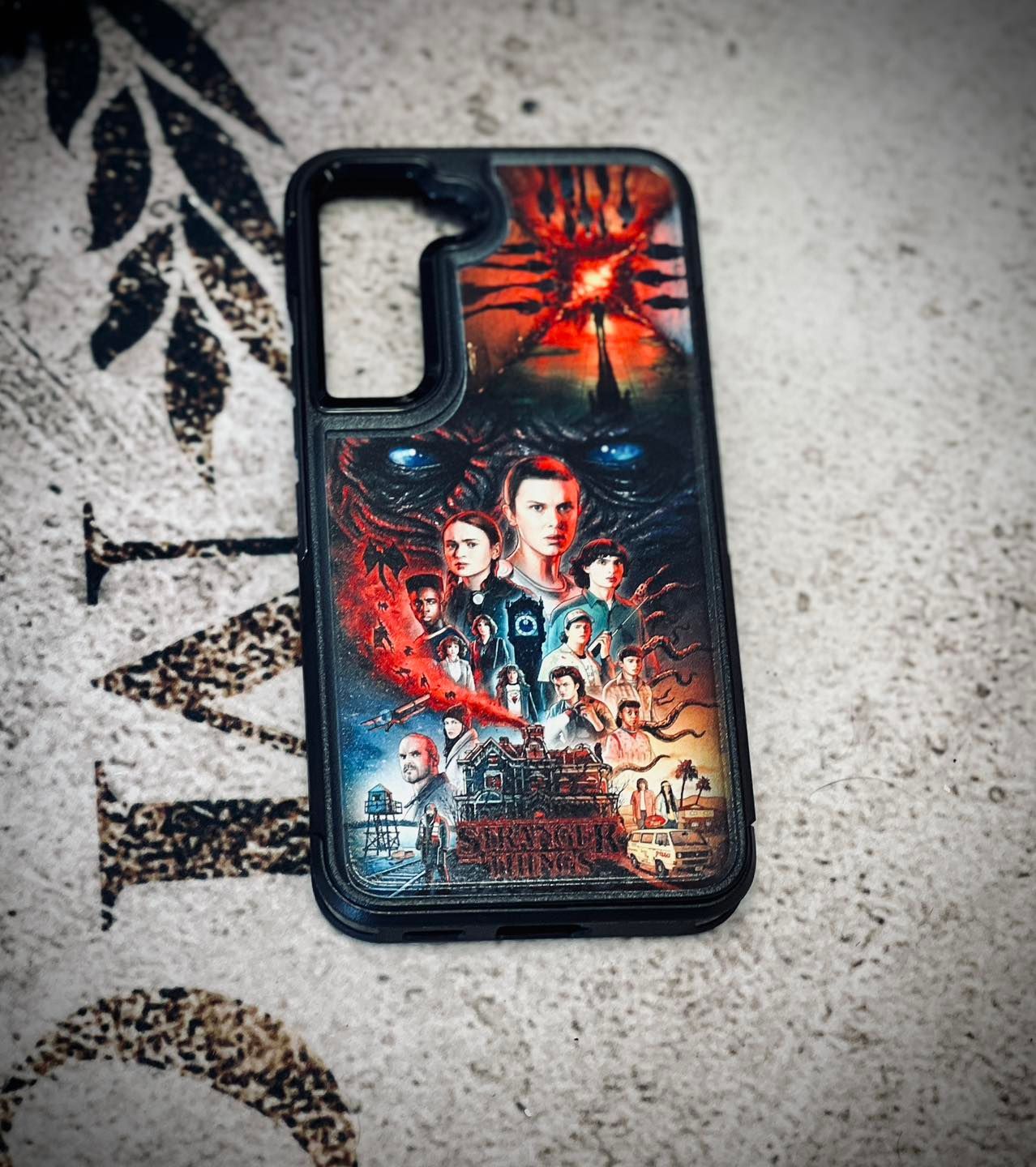 Black phone case with a Stranger Things-style graphic on a light textured surface.