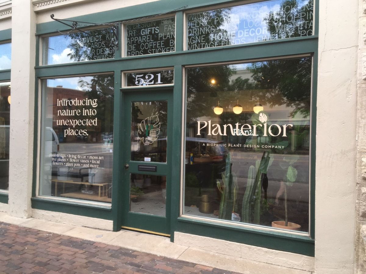 Storefront with green trim and large windows displaying the “Planterior” name and potted plants.