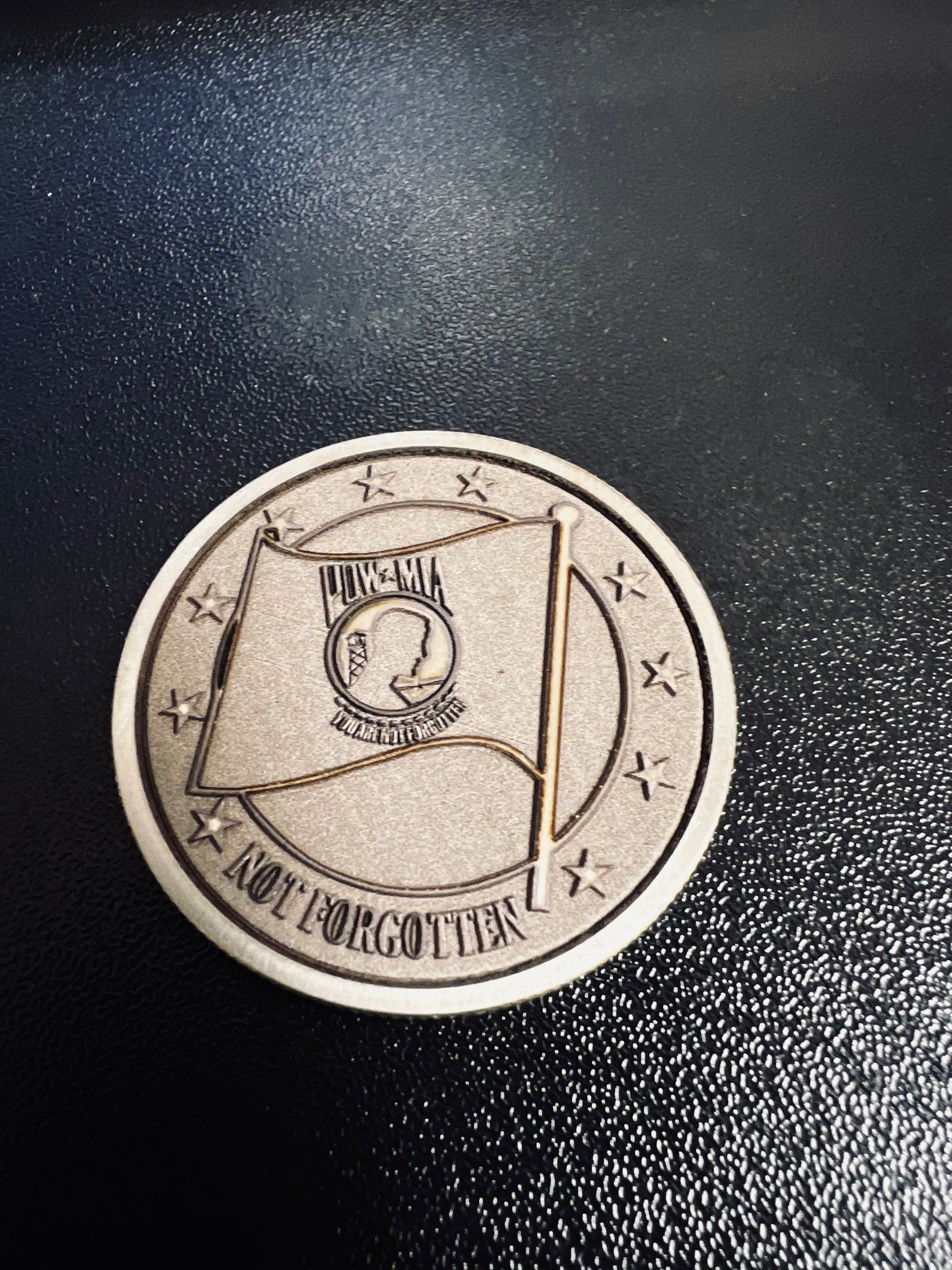 Silver coin or medallion with a flag-like emblem on a dark textured surface