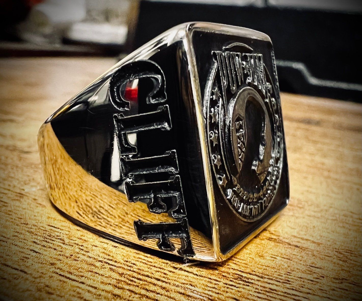 Black ring with a gold band and red gem, resting on a wooden surface.