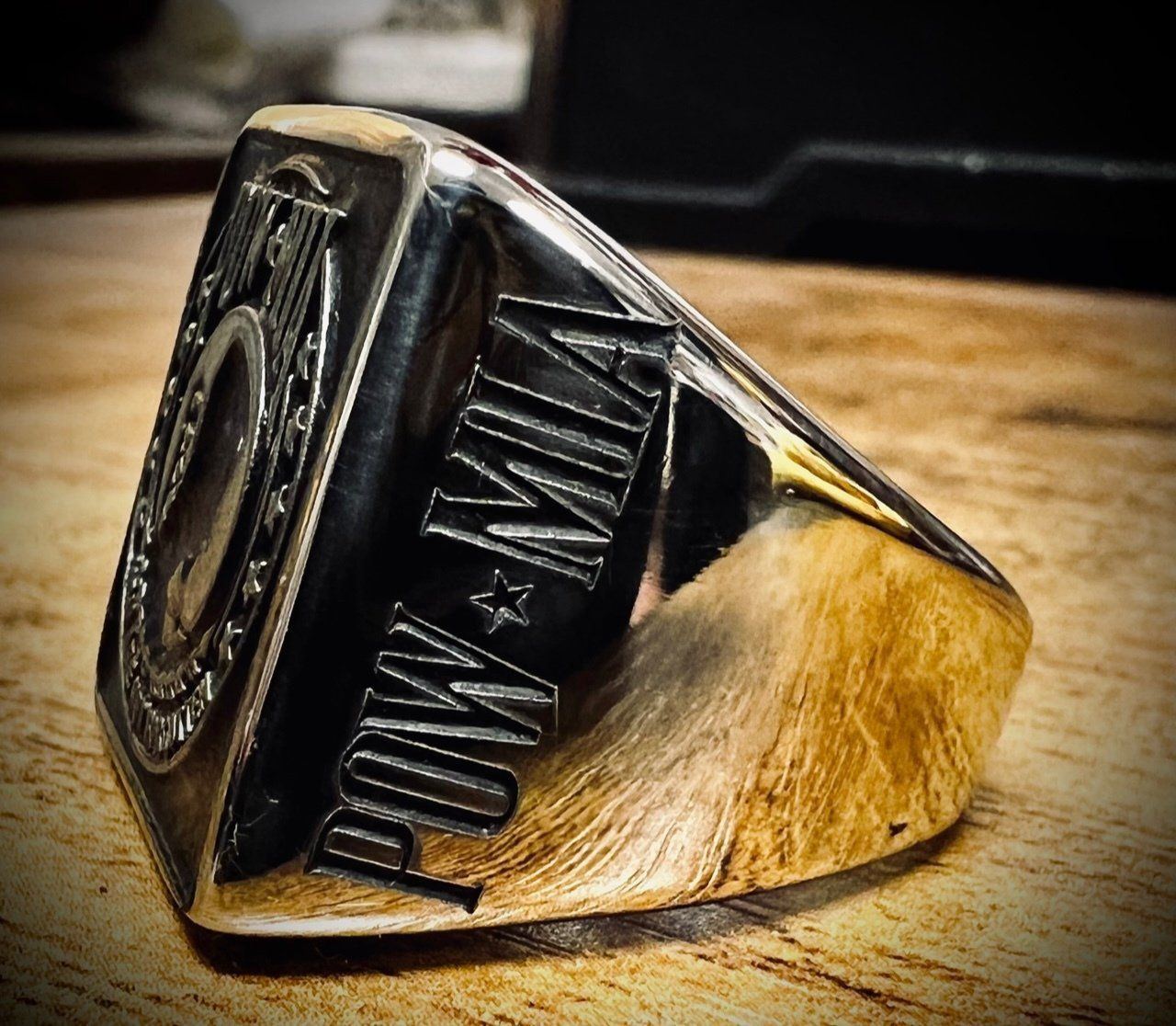 Close-up of a black and gold metal ring with engraved details on a wooden surface