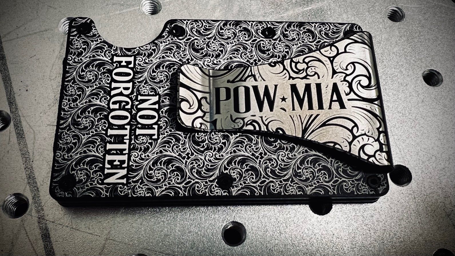 Black POW-MIA memorial plaque on stone ground with scattered bullets and “NOT FORGOTTEN” text