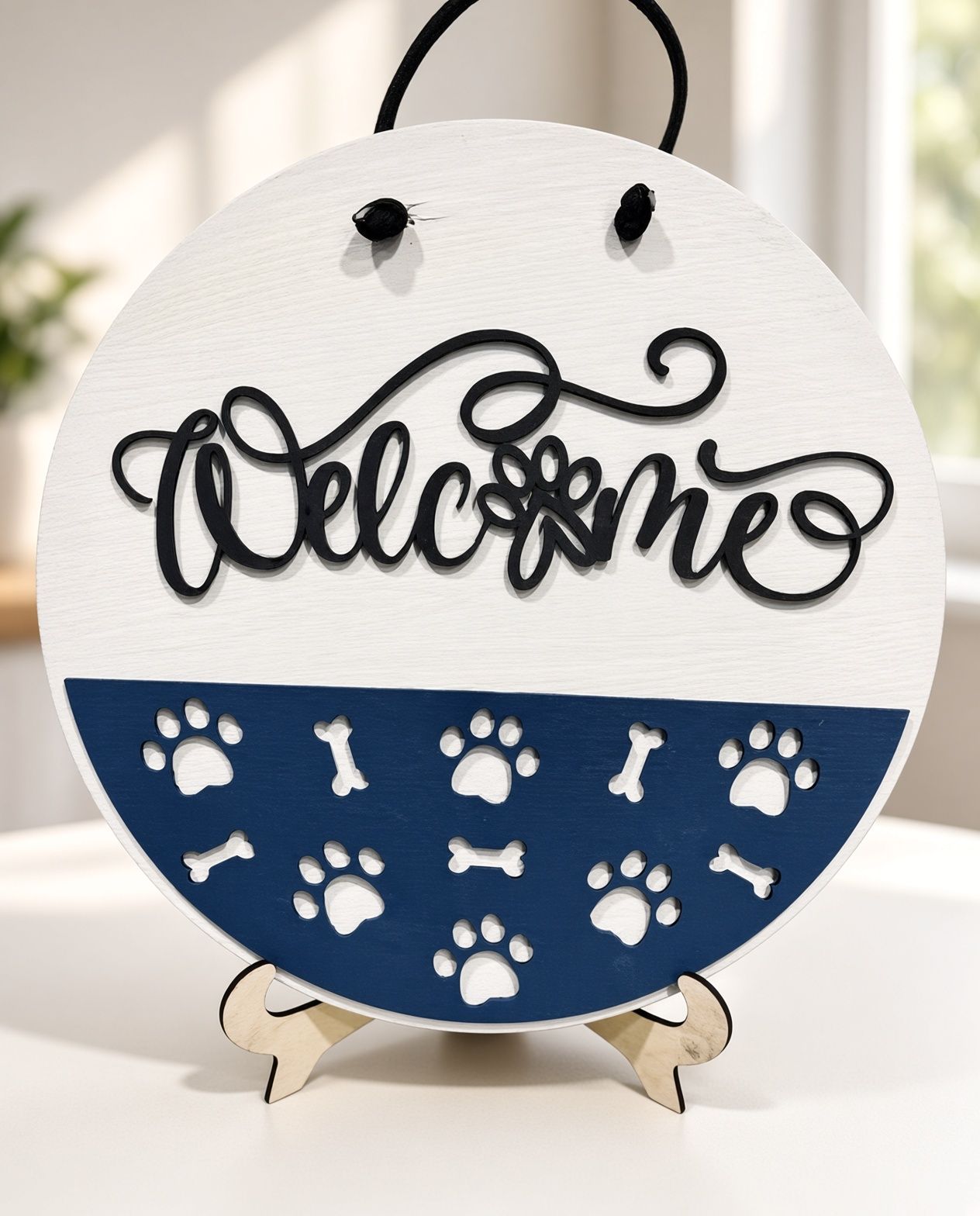 Round white-and-blue welcome sign with paw prints and bone accents on a small stand