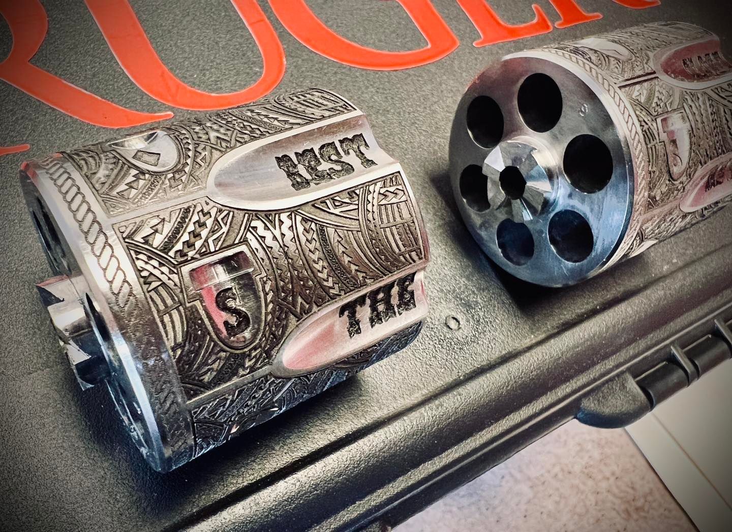 Two intricately engraved revolver cylinders, one with holes, on a gun case. The text 