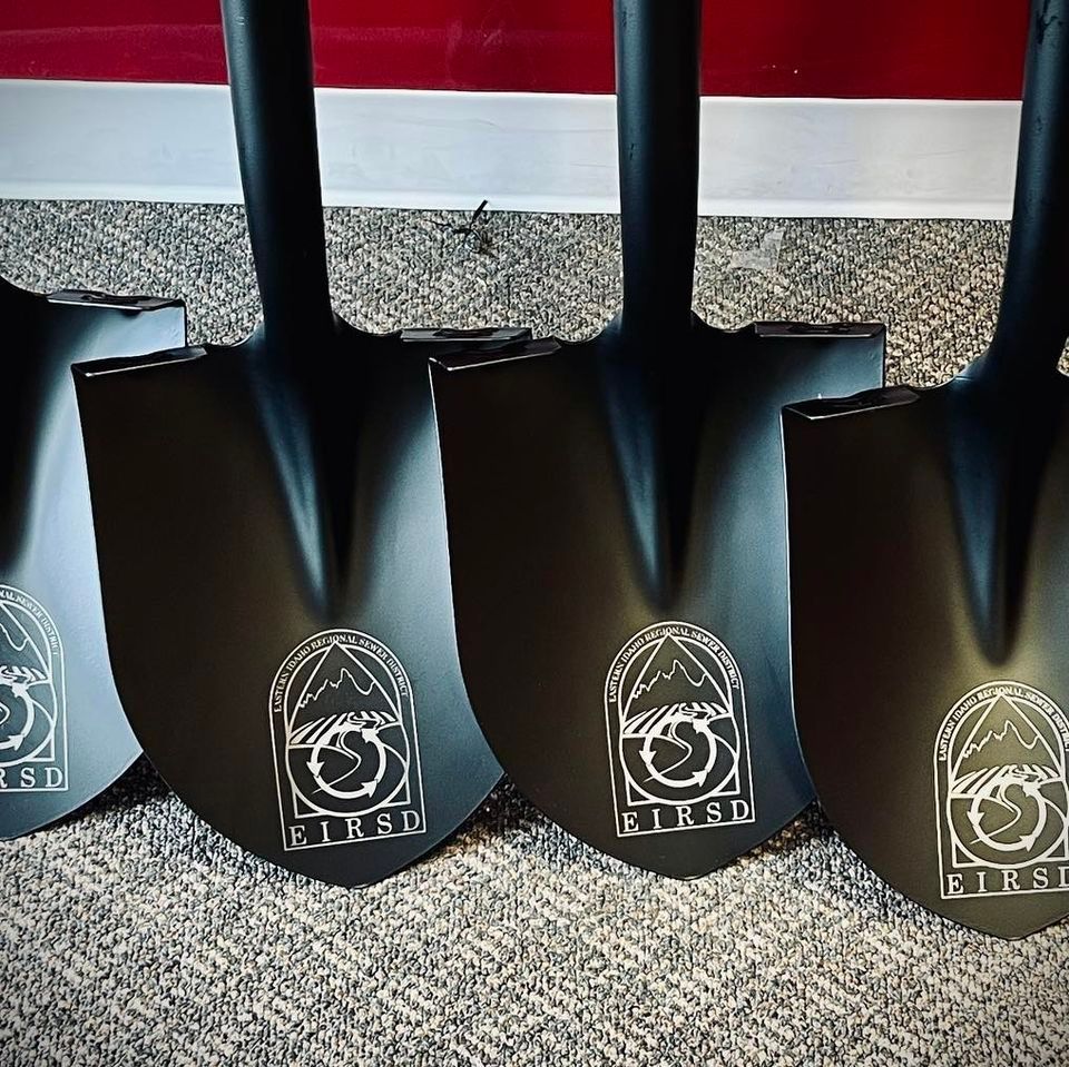 Four black shovels with white logo on blades, lined up against a wall.