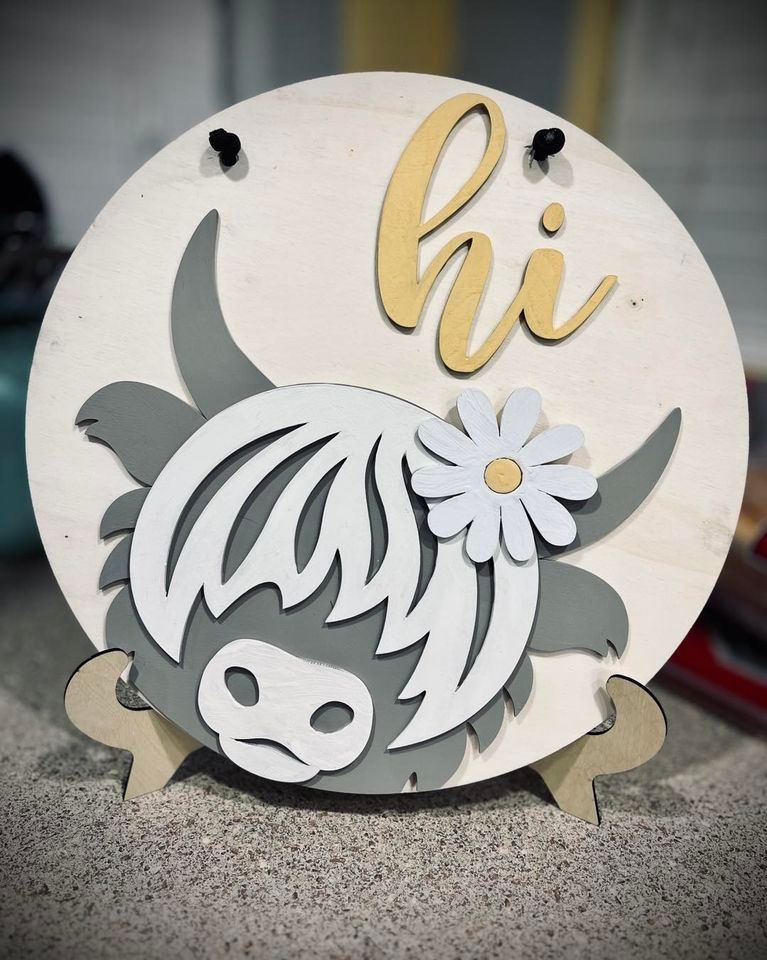 Wooden round sign with a gray and white highland cow, daisy, and 