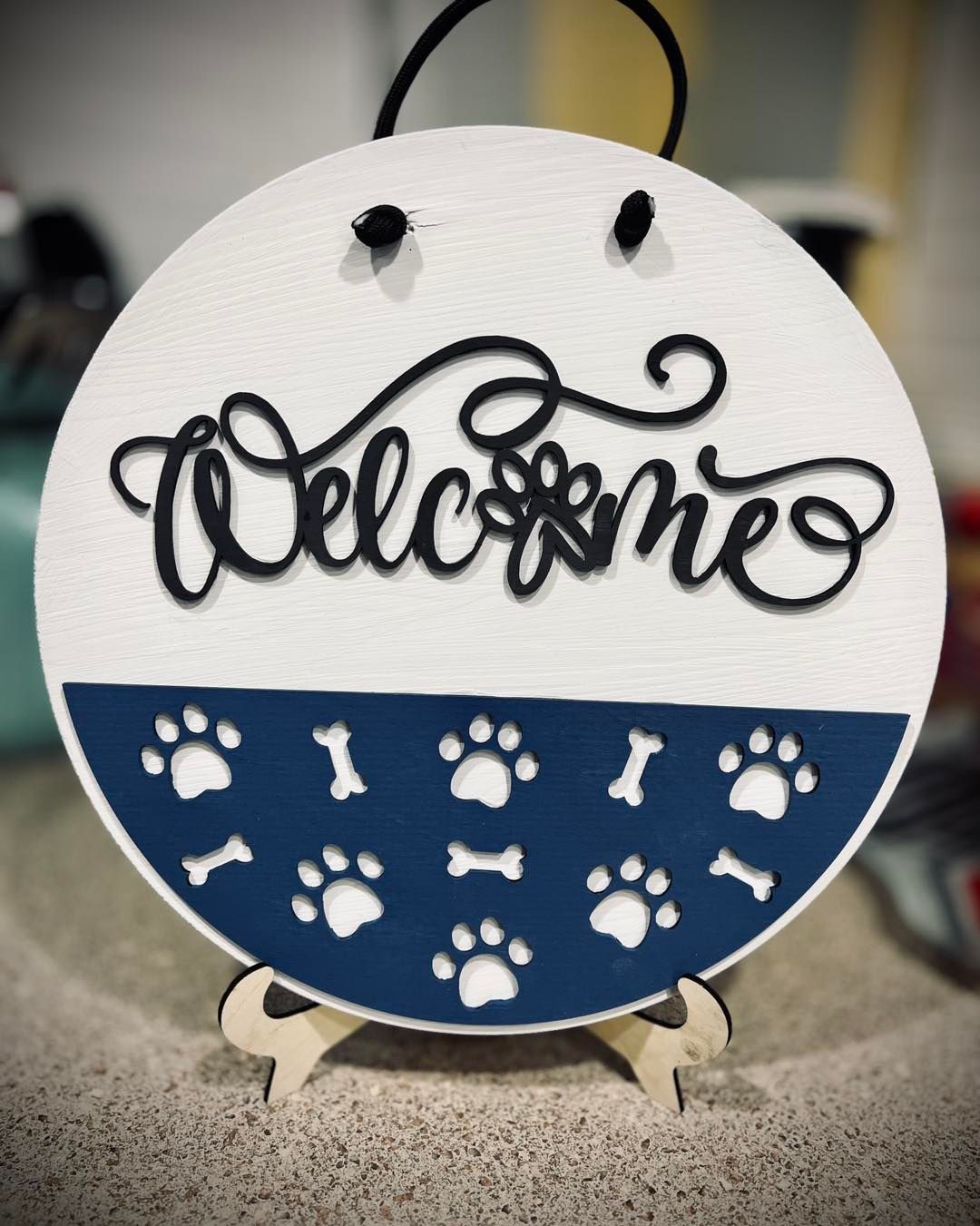 Round welcome sign for pets with paw prints and bones, white top, blue bottom.