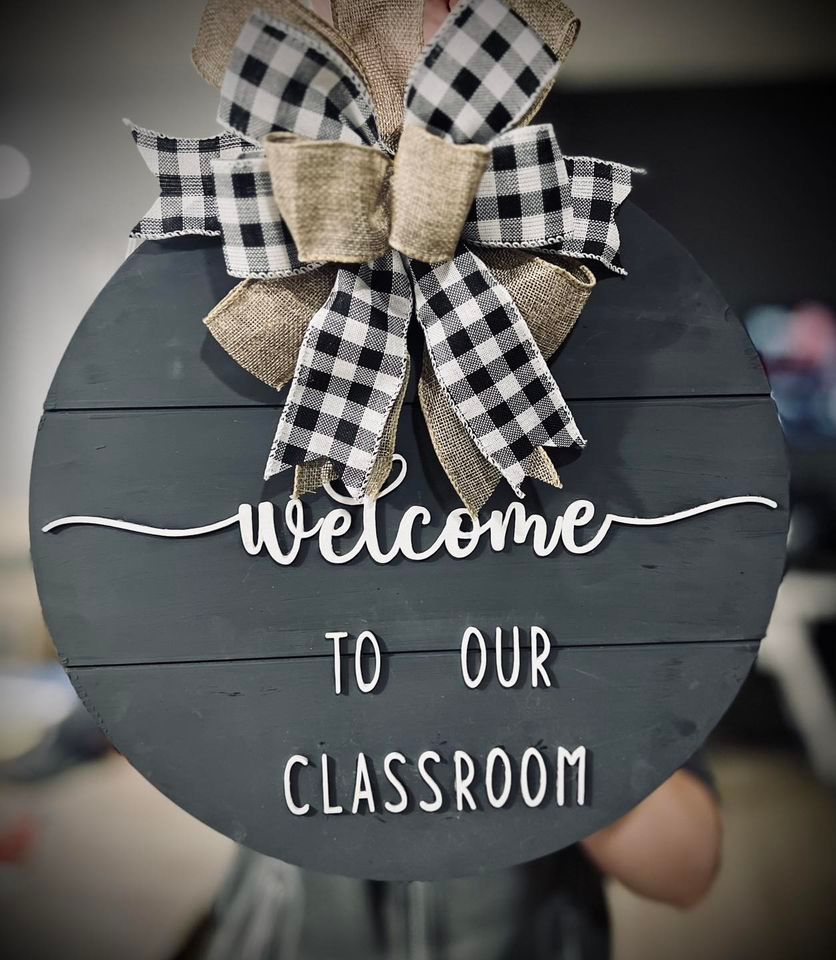 Round wooden classroom sign with black and white plaid bow; text reads 