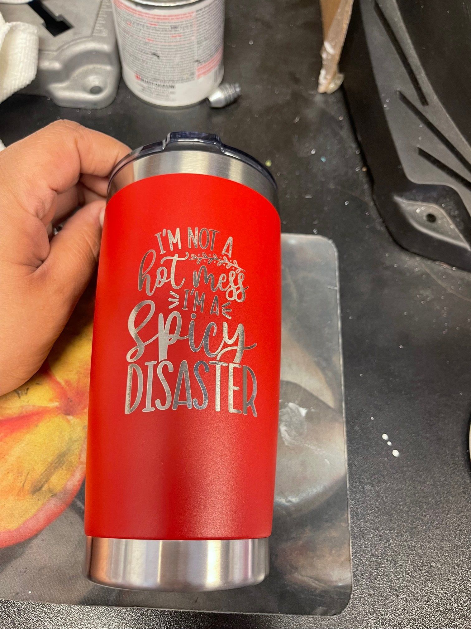 Red insulated tumbler with a silver top and bottom, held in a hand on a workshop table.