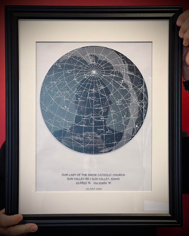 Framed celestial map with constellations and grid lines, held against a red background.