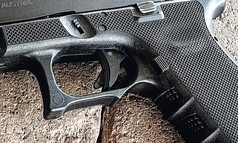 Close-up of a black handgun grip and trigger on a textured surface.