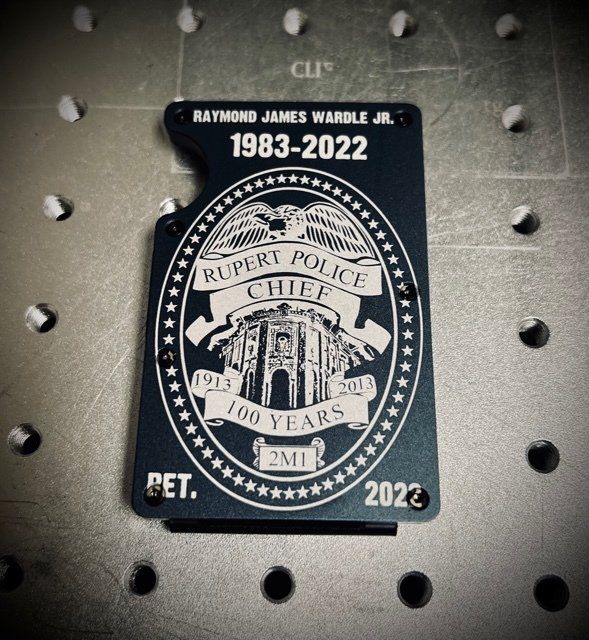 A dark blue police badge with white lettering. It commemorates Rupert Police Chief, Raymond James Warble Jr. (1983-2022).
