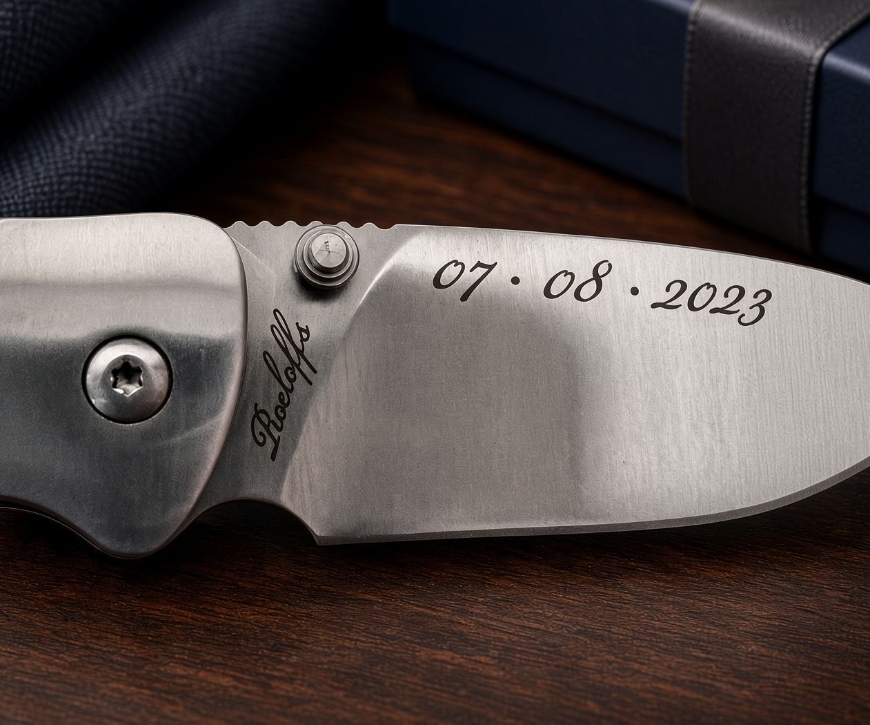 Close-up of a silver knife blade engraved with “07 08 2023” and a small signature