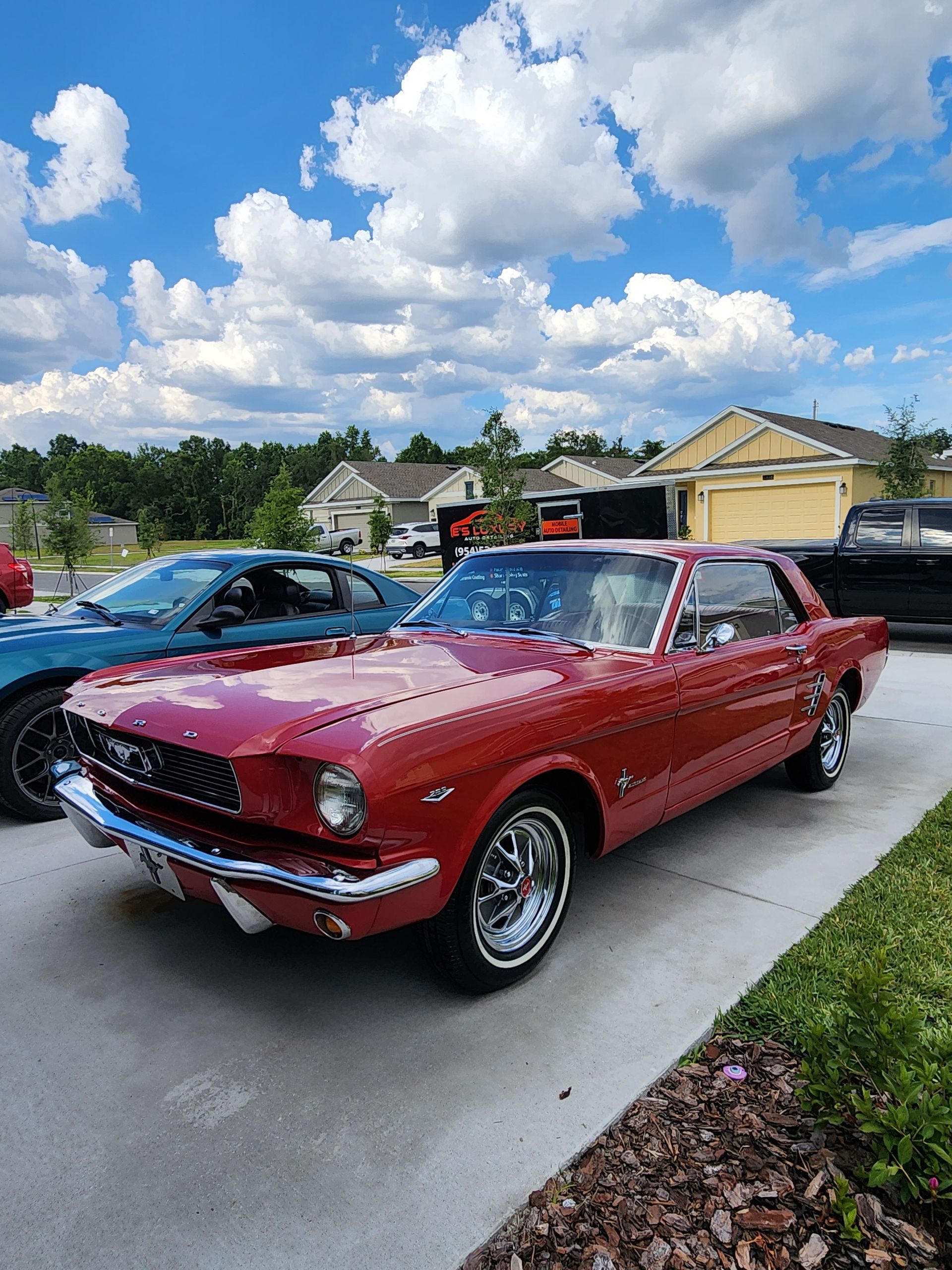 Red vintage Mustang parked on a driveway, blue sky and residential setting.