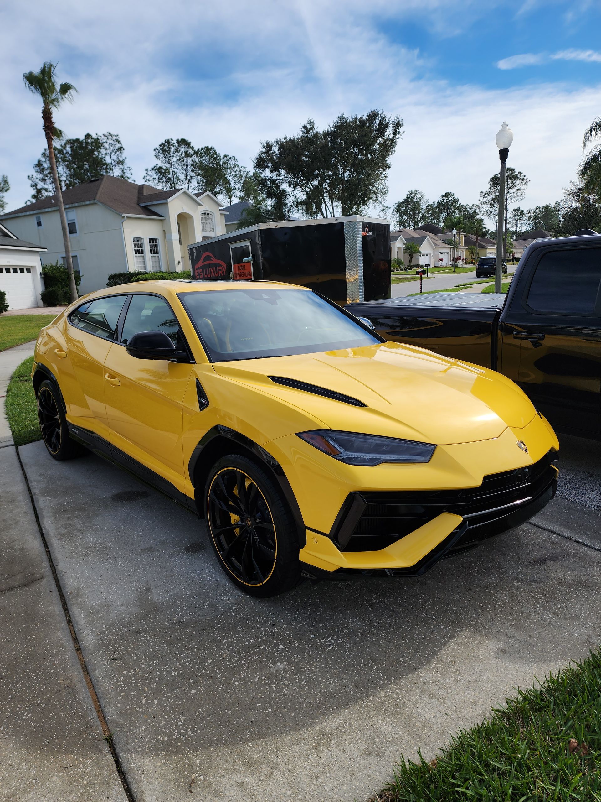 Yellow Lamborghini Urus SUV parked on a driveway in a suburban neighborhood.