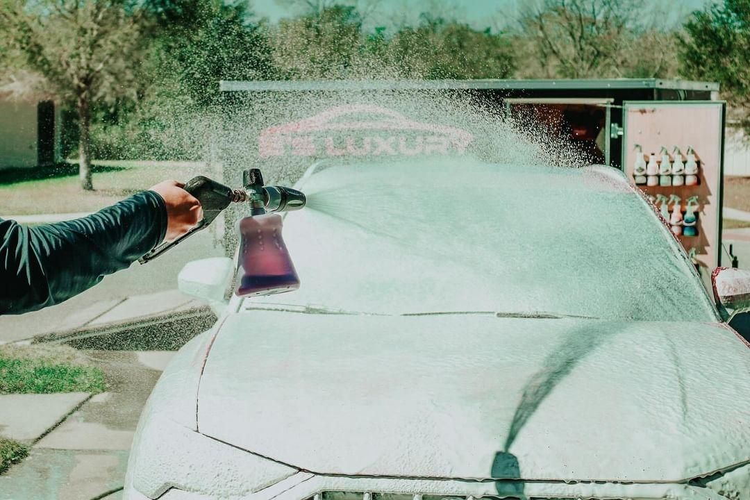 A person washing a white car with foam using a spray gun outdoors.