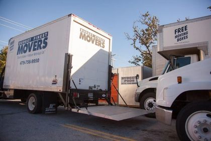 Two white moving trucks parked outdoors, with one truck's loading ramp lowered.