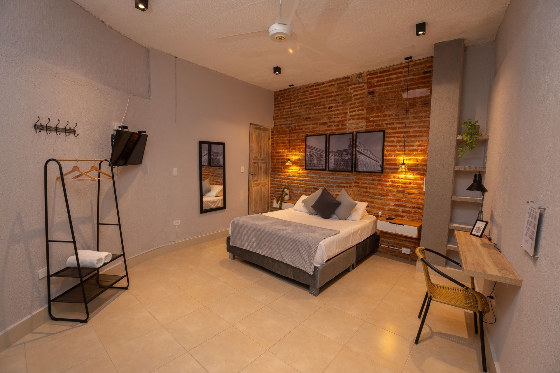 Bedroom with brick accent wall, bed, desk, clothing rack, and mirror.