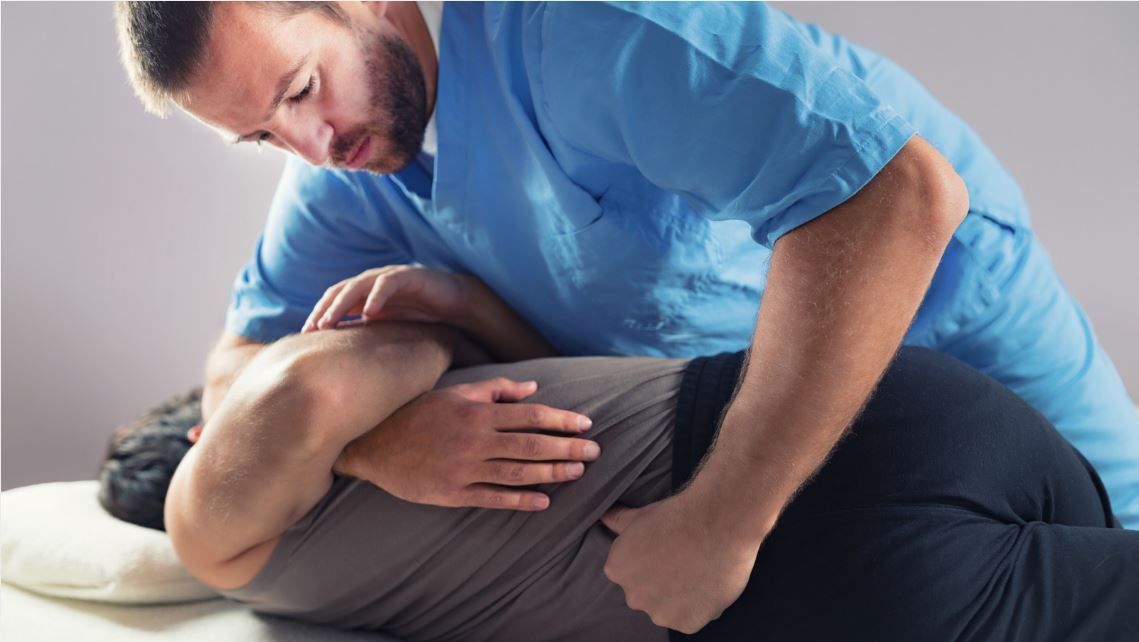 Chiropractic professional performing a spinal adjustment on a patient in a modern healthcare office with a city view background.