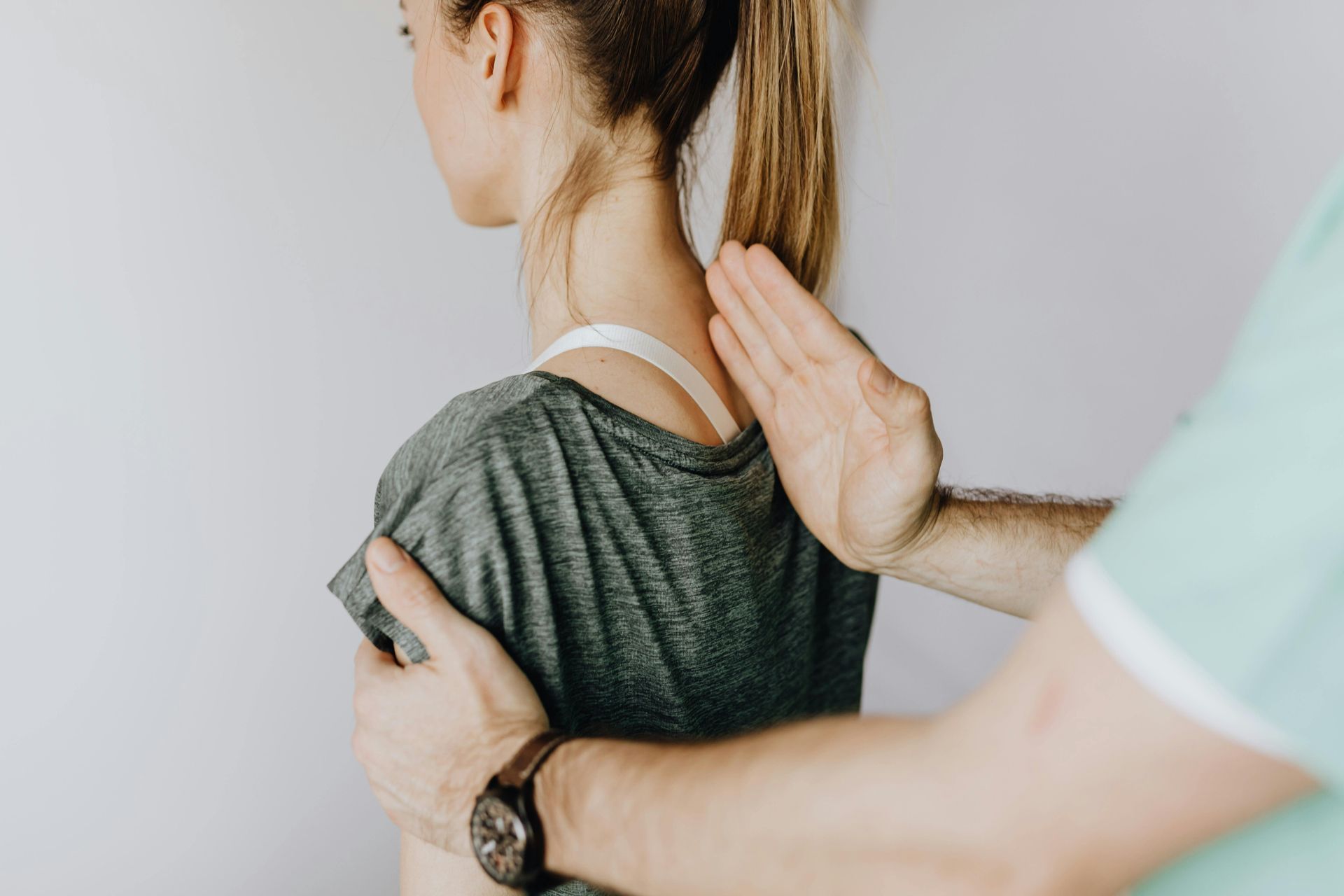 Chiropractor examining a woman's back and shoulders; hands visible, light setting.