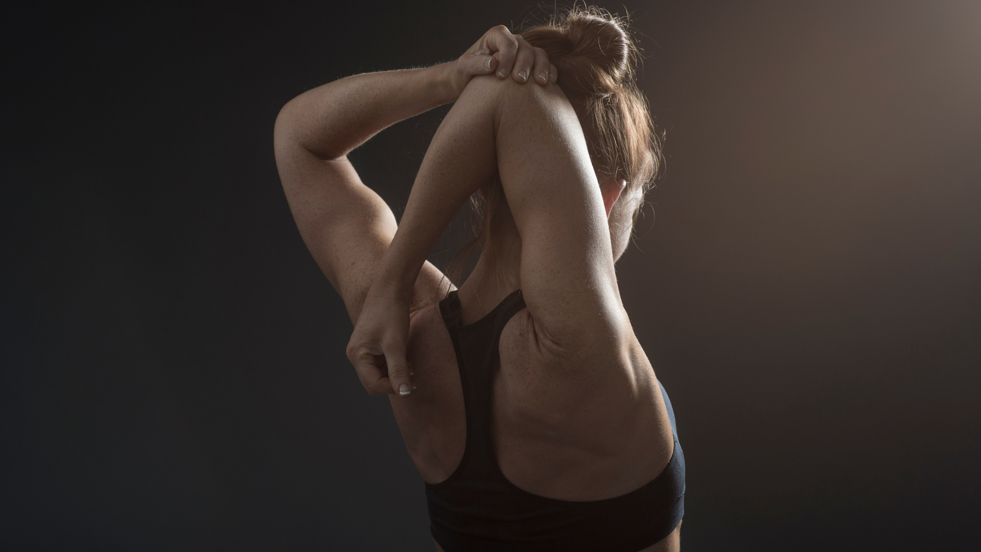 Person stretching with arms overhead against a dark background.