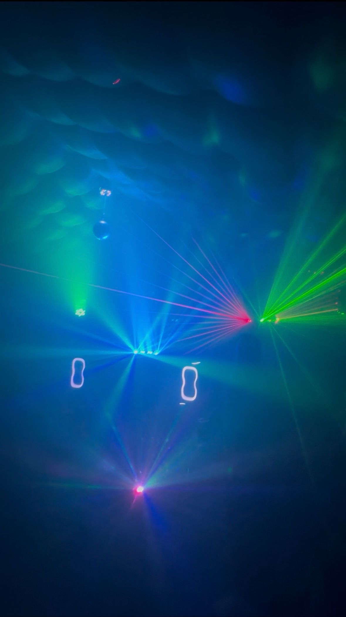 Twee zwarte laserprojectoren die rode, groene en blauwe lichtstralen op een donker oppervlak projecteren.