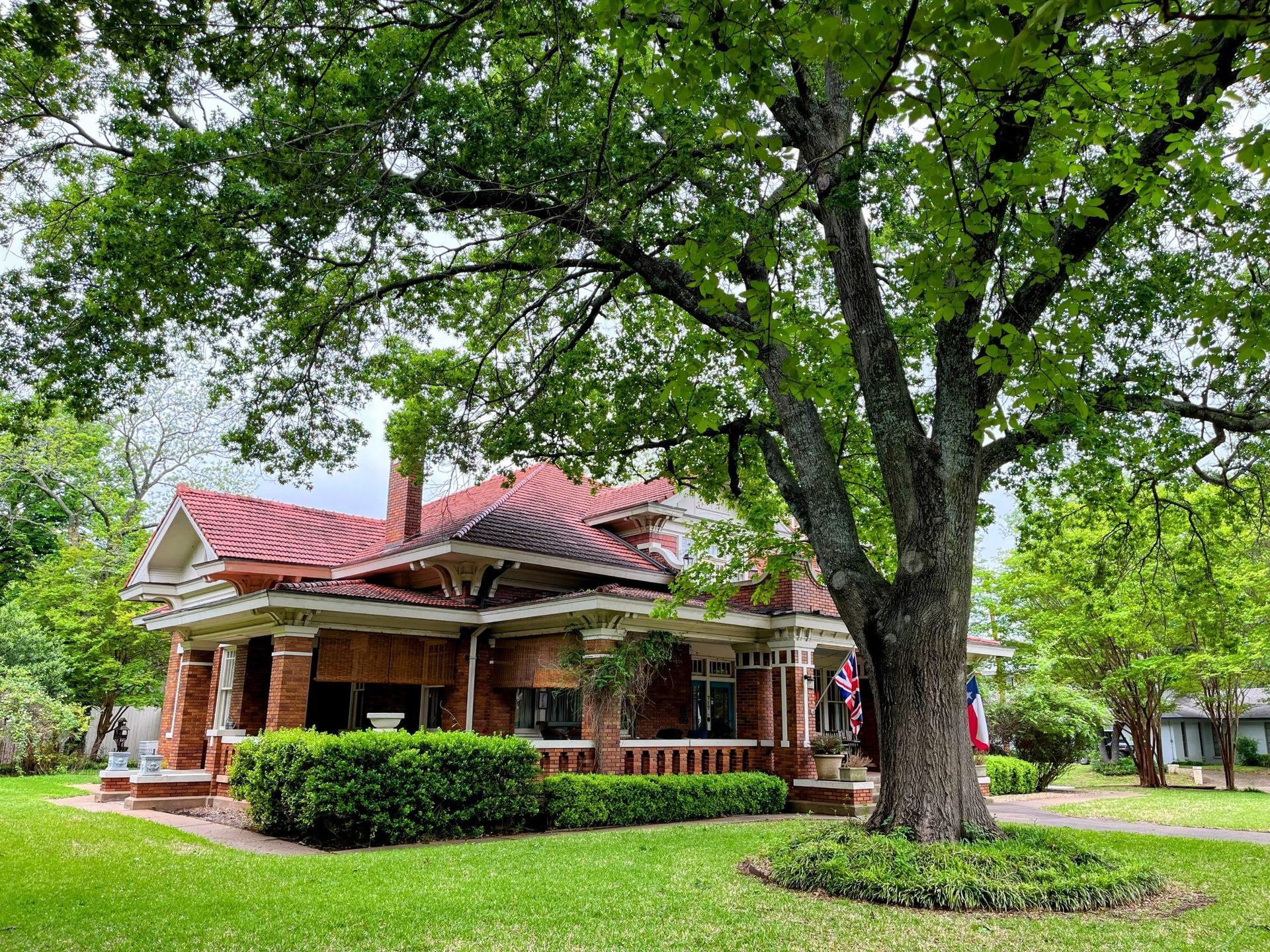 Red brick house with a tiled roof, surrounded by a green lawn and large tree.